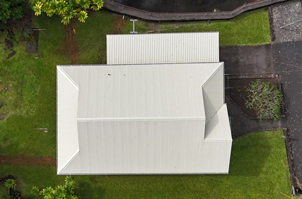 Aerial view of a residential house with a metal roof on a green lawn.